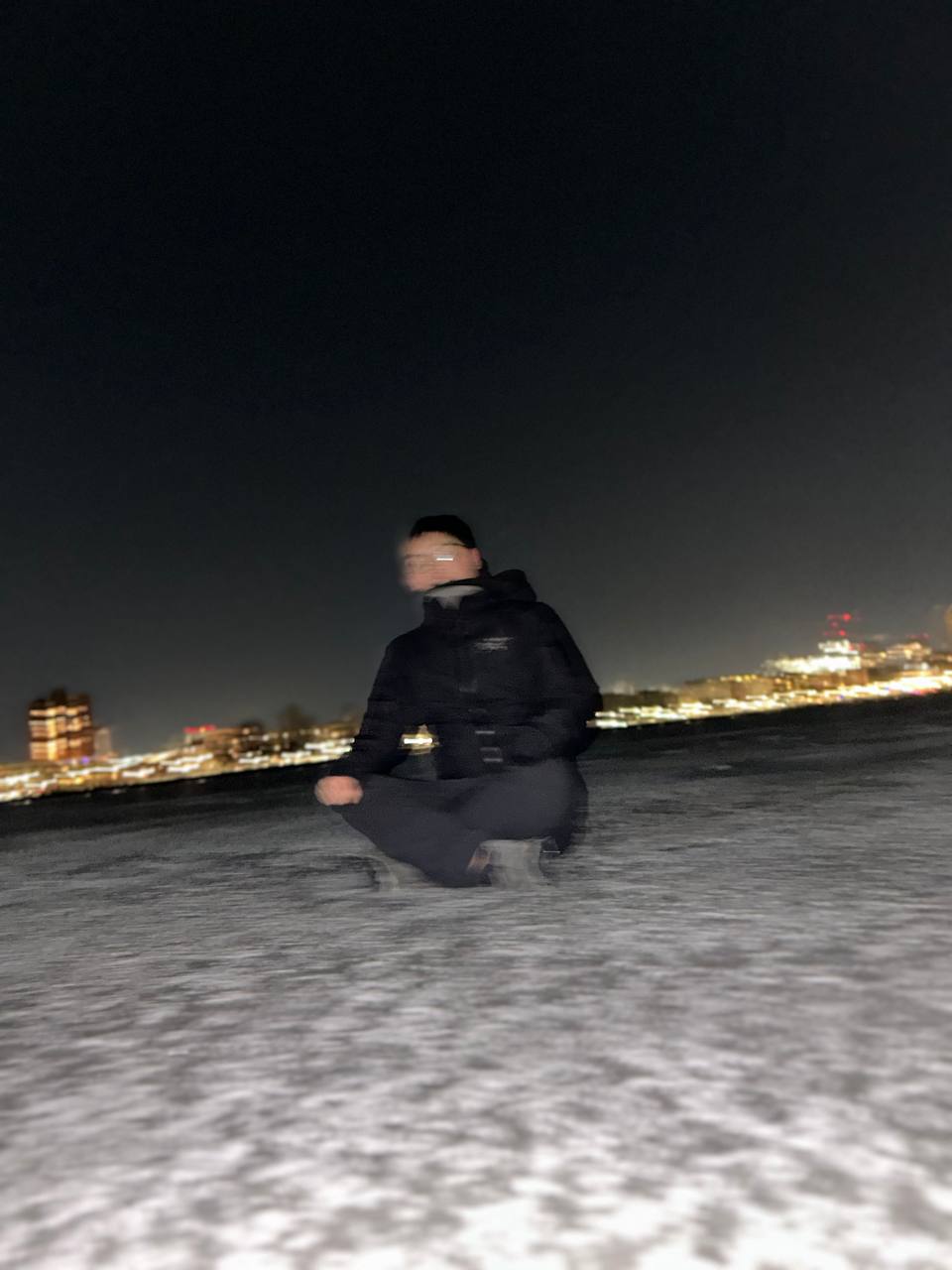 Jack meditating in lotus pose on a snowy rooftop at night, city lights behind him